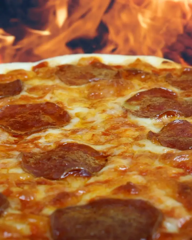 Pizza de pepperoni saliendo del horno a leña