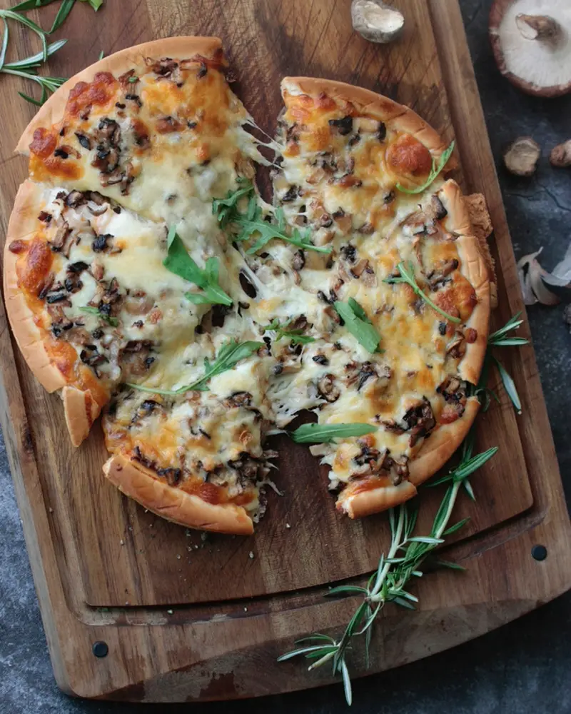 Pizza de hongos cortada sobre tabla de madera